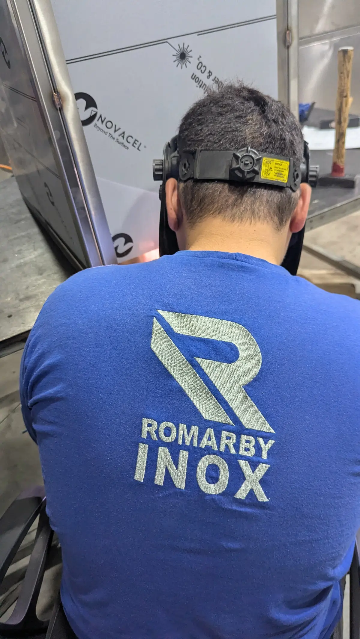 Sudor în echipament Romarby Inox, cu cască de sudură, văzut din spate, în atelier